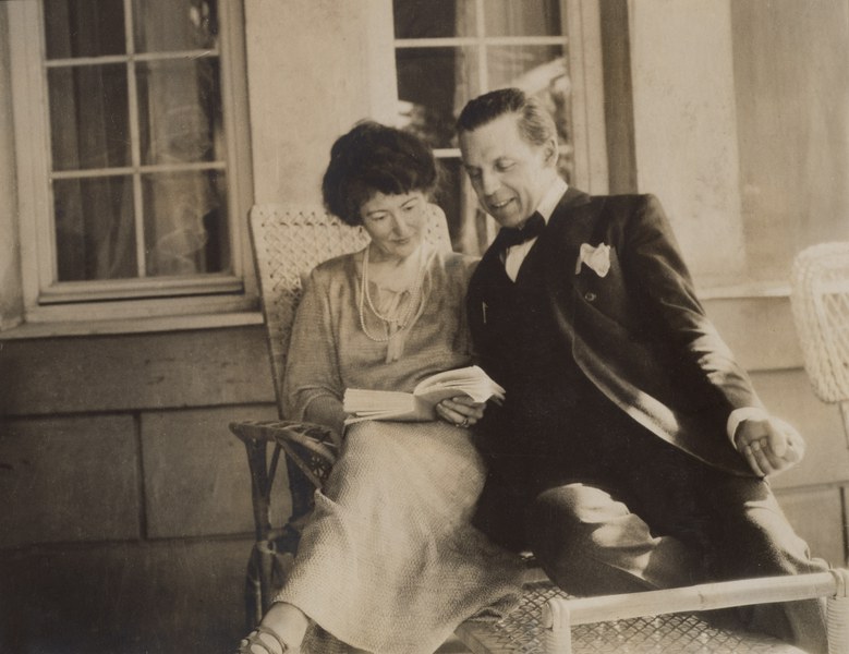 Mildred and Robert Bliss seated in front of windows reading together from a book