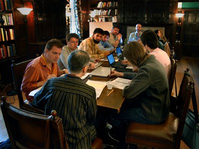 Group of summer school participants sitting at a long wooden table covered in papers and laptops