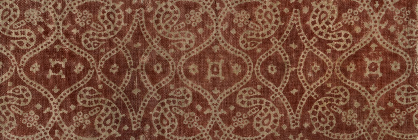 A textile fragment with a brick red background and block print sinuous design