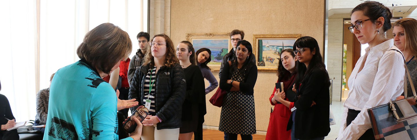 A group of students is standing in a gallery, listening to a guided tour