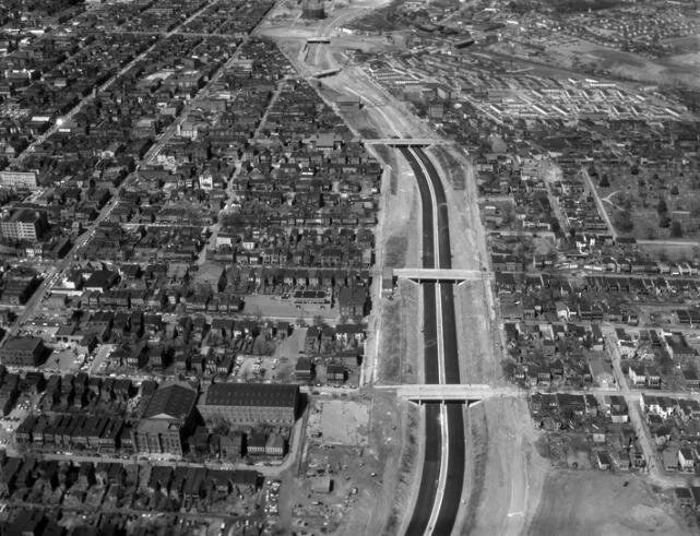 Black-and-white aerial view of a highway under construction running through the middle of a gridded city.