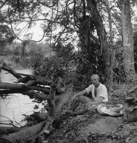 Robert Bliss seated among trees on the bank of a river