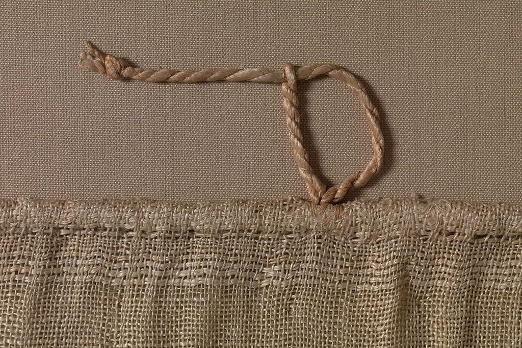  Detail of Hanging with Nikes Holding Bowl of Fruit, showing a linen cord sewn along the upper edge for the installation of the hanging