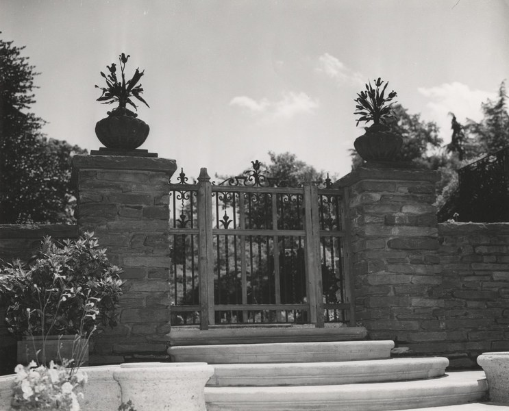 Two iron bouquets atop stone pillars with a wooden and iron gate between