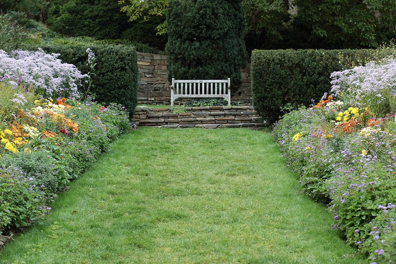 A grass pathway, bordered by plantings, terminates in stone stairs, a teak bench, and a large yew, named Mrs. Yew.