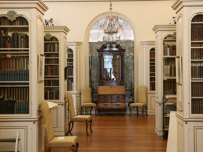 Large room with several rows of ornate white bookcases on both sides of a wide aisle dotted with yellow highback chairs
